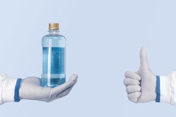 Alcohol antiseptic and disinfectant bottle in a hand and showing thumb up of healthcare workers on blue color background