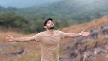 Man enjoying feeling carefree freedom with open arms over nature background in the morning. Bearded man eyes closed standing breathing fresh air on top of mountain.