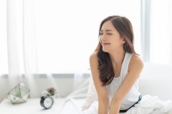 Beautiful Asian Smiling woman with eyes closed relaxing in bed at home. Portrait of Happy Charming Shy girl in white pajamas with long hair wake up and breathing air on morning. Carefree, Positive emotion, Expression face.