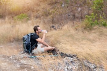 Portrait Tired man traveler in black shirt drinking water. Male backpacker sitting relaxing on top of mountain in beautiful trail in countryside. copy space.