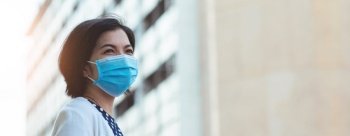 Young Asian woman wearing protective face mask looking something in new normal life while pandemic covid-19 or coronavirus against building background in the city at outdoor, Panoramic, Banner