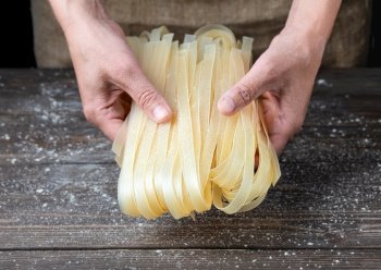 Female hands hold cooked noodles. Cooking noodles at home, close-up, dark wooden background, flour scattered on the table.. Female hands hold cooked noodles.