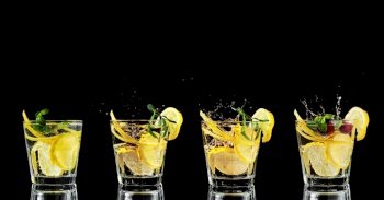 Four glass with lemonade or mojito cocktail with lemon and mint. Cold drinks on a black background. Splashing ice falling into glasses. Copy space, close up.