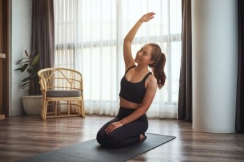 Closeup image of a beautiful young asian woman sitting on training mat and stretching her arms to warm up before workout at home