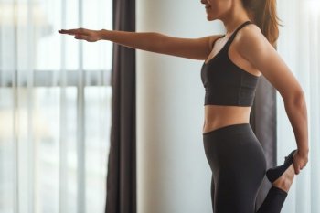 Closeup image of a fitness woman stretching her leg and arm while warming up before workout at home