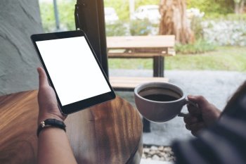 Mock up image of hands holding black tablet pc with white blank screen while drinking coffee in cafe