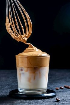 Iced Dalgona Coffee with Corolla on Dark Background. Trendy Creamy Whipped Coffee. South Korean Cold Summer Drink.. Iced Dalgona Coffee with Corolla on Dark Background. Trendy Creamy Whipped Coffee. South Korean Cold Summer Drink