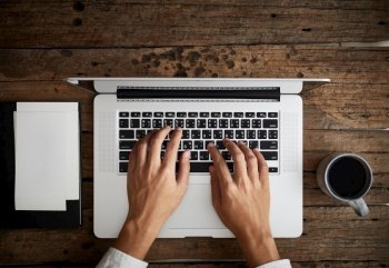 A man is typing on laptop keyboard on modern white office desk, top view
. A man is typing on laptop keyboard on modern white office desk
