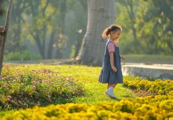 Soft blur image of little Asian girl look happy to play among flower garden with morning light.