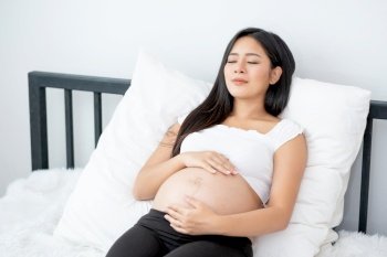 Beautiful Asian pregnant woman lie on bed and look relax with morning light in bedroom. Concept of good healthy activity for mother and support growth of baby in belly of people.