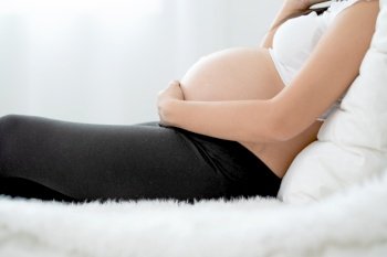 Beautiful Asian pregnant woman lie on bed and use hand touch belly with carefully emotion. Concept of good healthy activity for mother and support growth of baby in womb of people.