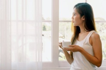 Young asian woman having a cup of coffee. She stay isolation at home for self quarantine. Corona virus outbreak situation. Self quarantine at home prevention COVID-19.