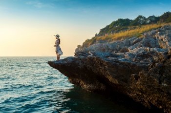 Young woman standing on the top of rock and looking at the seashore and sunset in Si chang island.