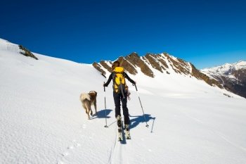 Woman with her faithful dog in the mountains during a ski mountaineering trip.