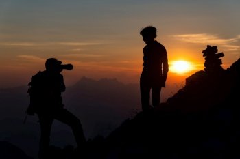 Photographer performs photography to a girl at sunset in high mountains in silhouettes.