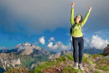 Girl in the summit at the mountain raises her arms happy.