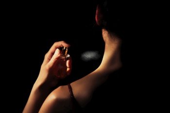 Woman sprays perfume on her neck with a black background.