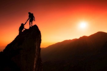 Team of climbers help to conquer the summit in teamwork in a fantastic mountain landscape at sunset