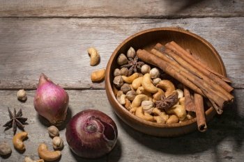 Low key of image of Selection of dried fruits, nuts cinnamon sticks, anise stars and brown sugar in a vintage wood cups on a dark textural wooden background.