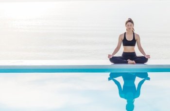 Asian woman practice yoga lotus pose on the pool above the beach in the morning,Feeling so comfortable and relax in holiday