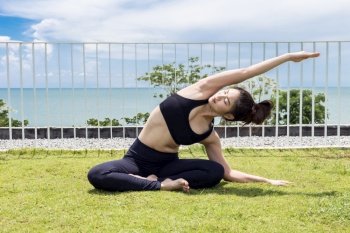 Happy Asian woman wearing black sport wear practice yoga Seated side stretch pose with beautiful sea,Feeling relax and comfortable,Healthy Concept