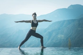 Beautiful Attractive Asian woman practice yoga warrior or Virabhadrasana Pose on the pool above the Mountain peak in the morning in front of beautiful nature views in SAPA vietnam,Feel so comfortable