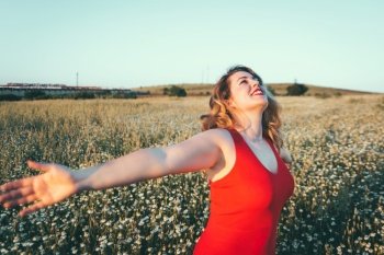 woman in red dress enjoying freedom in a field of daisies