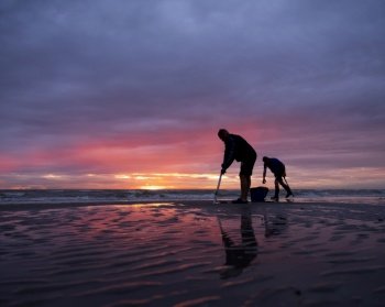 men on normandy beach during colorful sunset look for worms to use as bait for fishing
