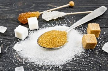 Brown granulated sugar in a metal spoon, white granulated sugar on a table, crystalline and cubes on black wooden board background