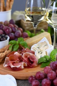 Antipasto. Wine set snacks of dried ham, camembert cheese with mold, parmesan with grissini, olives and pink grapes.