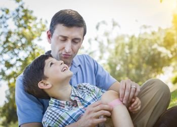 Loving Father Puts a Bandage on the Knee of His Young Son in the Park.