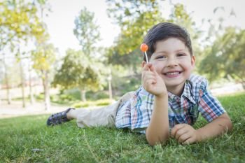 Handsome Young Boy Enjoying His Lollipop Outdoors on the Grass.