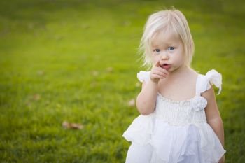 Adorable Little Girl Pointing At The Camera Wearing White Dress In A Grass Field.