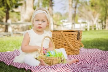 Cute Baby Girl Enjoys Enjoying Her Easter Eggs on Picnic Blanket in the Grass.