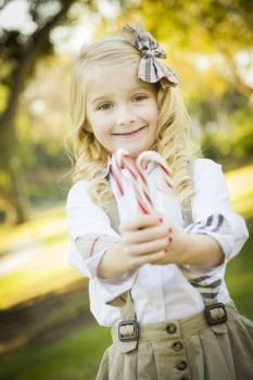 Cute Little Girl with a Bow in Her Hair Holding Her Christmas Candy Canes Outdoors.
