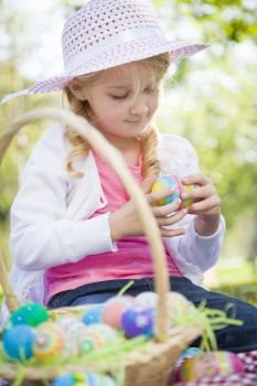 Cute Young Girl on Picnic Blanket Wearing Hat Enjoys Her Easter Eggs Outside in the Park.
