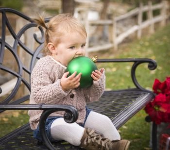 Happy Young Toddler Child Sitting on Bench with Large Christmas Ornament Outside.