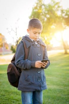 Young Hispanic Boy Walking Outdoors With Backpack Texting on Cell Phone.