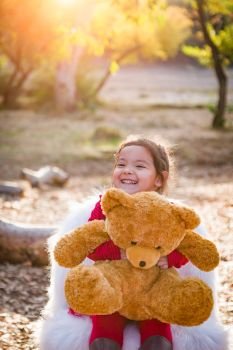 Cute Young Mixed Race Baby Girl Hugging Teddy Bear Outdoors.