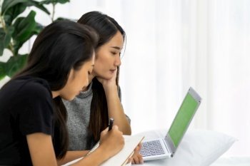 Two Asian university woman using laptop book at home in bedroom for studying while School shutdown due to city lockdown from COVID-19 Pandemic. Education online and study at home concept.