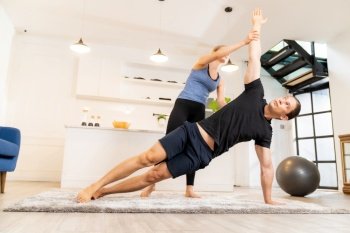 White caucasian man learning yoga at home. Female instructor or trainer coaching and adjust correct side plank pose to student. Workout healthy lifestyle and Yoga health delivery concept.