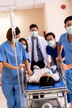 Seriously injured patient with oxygen mask on gurney stretcher bed pushed by medical team of doctor nurse and paramedic to the Operating Room. Emergency health care and medical hospital concept.