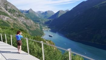 Tourism holidays pictures and traveling. Mature female tourist enjoying scenic fjord landscape Geirangerfjord from Ornesvingen viewpoint, taking photo with camera, Norway Scandinavia.. Tourist taking photo of fjord landscape, Norway