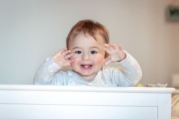 Portrait of a cute little baby boy at home in the crib making faces, sweet child having fun in his bedroom, happy healthy childhood 