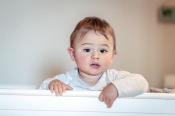 Portrait of a cute little boy standing in the crib in kids bedroom, pretty adorable baby wearing pajamas, happy healthy childhood
