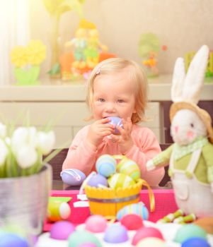 Adorable playful little girl coloring eggs for spring religious holiday, sitting near bunny toy, celebrating Easter at home