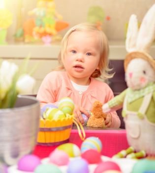 Cute little baby girl painting eggs in different colors near traditional Easter bunny, art lesson in daycare, celebrating happy spring holiday