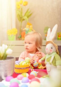 Adorable little girl paint eggs for spring religious holiday, sitting near bunny toy, celebrating Easter at home
