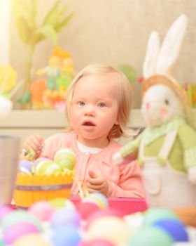 Cute little baby girl painting eggs in different colors near traditional Easter bunny, art lesson in daycare, celebrating happy spring holiday