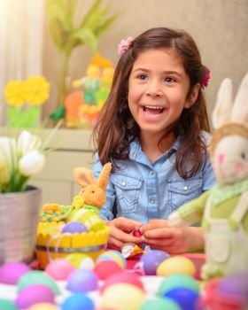 Portrait of cute little girl playing in daycare, painting eggs in different colors, with pleasure preparing to happy Easter holiday